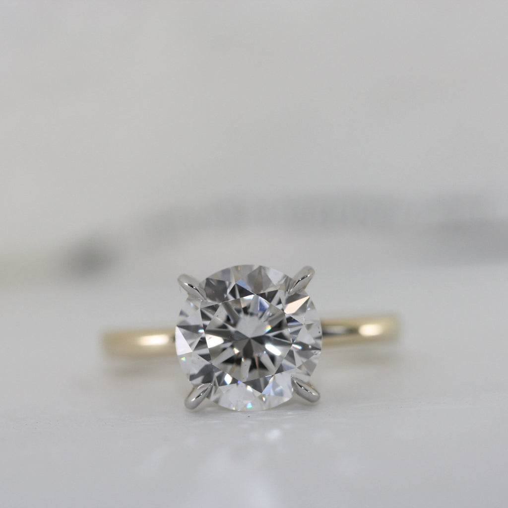 This stunning engagement ring features brilliant 4 carat round lab grown diamond set in white gold setting, beautifully complemented by a yellow gold shank. Two tone design enhances the diamond brightness creating outstanding 